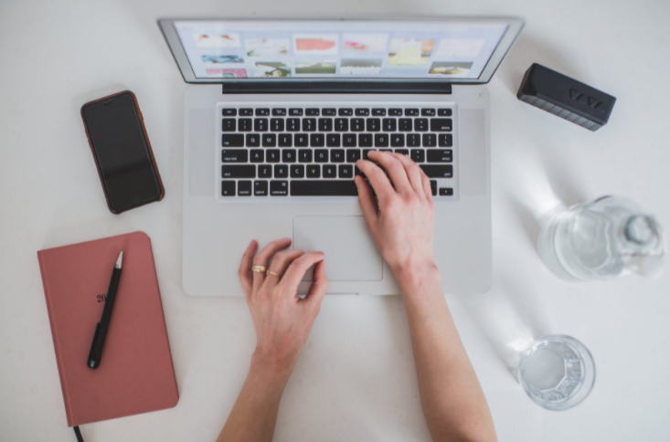 pessoa mexendo em laptop com celular e um bloco de notas ao lado